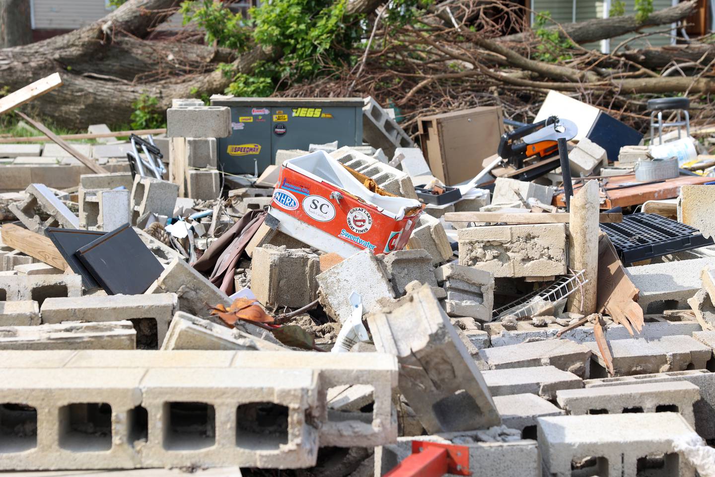 Personal belongings lay scattered among the rubble at the site of Sue Antonelli's former Sandbar Road home on May 19, 2026, following the March 10 tornado that leveled her Aroma Township property. A cooler displays a sticker for South Carolina, where she and her late partner, Joe Tallman, would vacation to each year.