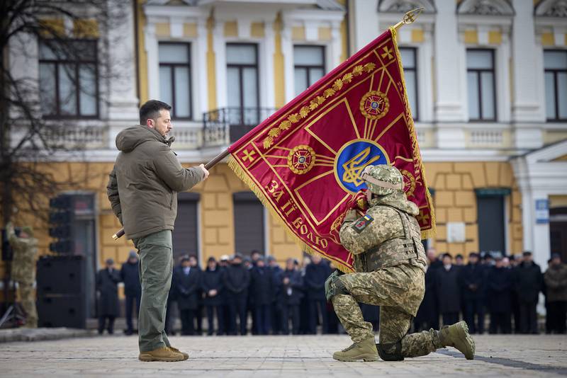 Ukrainian President Volodymyr Zelenskyy, left, holds the flag of a military unit as an officer kisses it, during commemorative event on the occasion of the Russia Ukraine war one year anniversary in Kyiv, Ukraine, Friday, Feb. 24, 2023. (Ukrainian Presidential Press Office via AP)