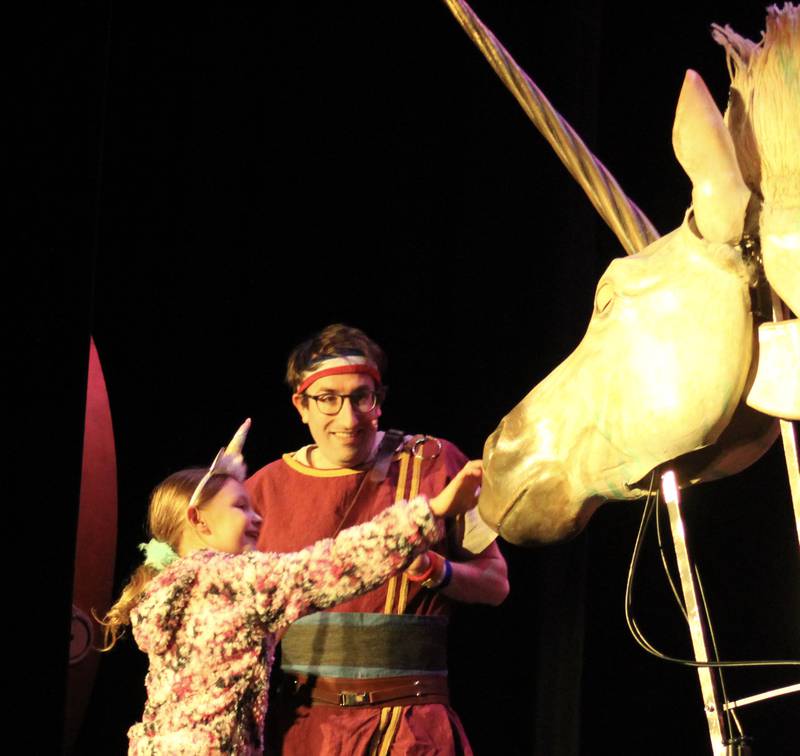 Dave the Hero Trainer guides a member of the audience into approaching an immense unicorn puppet as part of the "Dragons and Mythical Beasts" children's stage show on Saturday, Feb. 11, 2023 at Dixon Theatre.