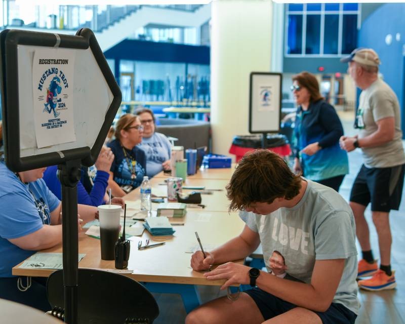 Mustang Trot participants sign up on race day and look for their packets before the race on Sunday April 14, 2024, held at Downers Grove South High School.
