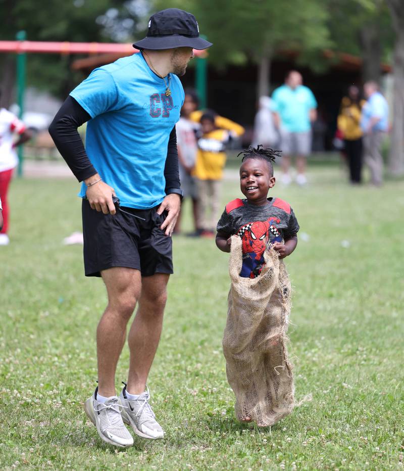 Trey Urwiler, a camp councilor at Camp Power encourages a participant in the sack race Tuesday, July 18, 2023, at Welsh Park in DeKalb. Camp Power, which is run by the Kishwaukee Valley YMCA, is a summer program for youth at University Village that provides positive activities for kids.