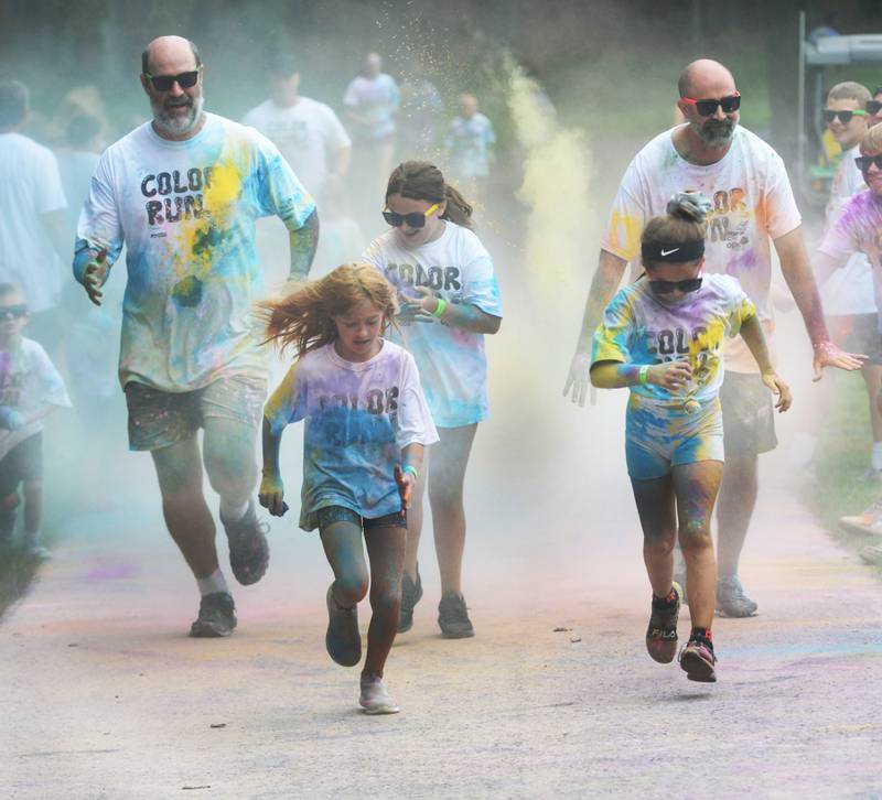 A family runs through one of the color stations at the Oregon Park District's color run on Tuesday, July 30, 2024. Runners and walkers got doused with powdered colors as they made their way along the course at Oregon Park West.