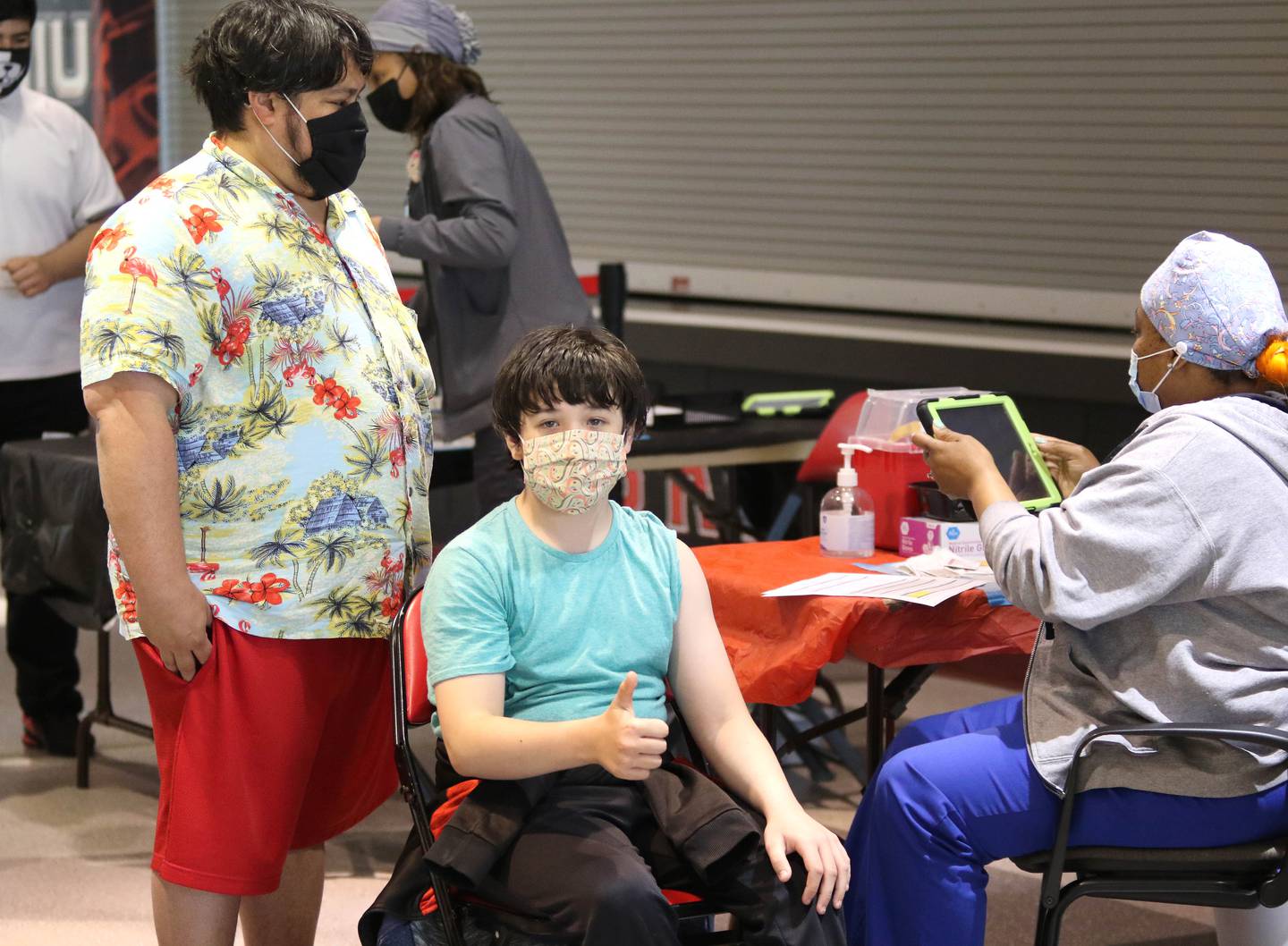 Henry Williams, 12, from Sycamore, with his dad Noel, gives a thumbs up prior to receiving his first shot of a COVID-19 vaccine from nurse Tvionne Watkins Thursday afternoon at the Convocation Center at Northern Illinois University in DeKalb.