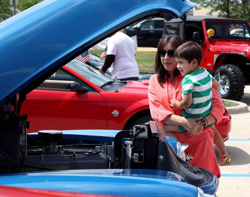 Teddy, 2, and Krystal Barnes, from Geneva, look at the motor of one of the cars Saturday, June 14, 2025, after the Flag Day Car Show in the Hy-Vee parking lot in Sycamore.