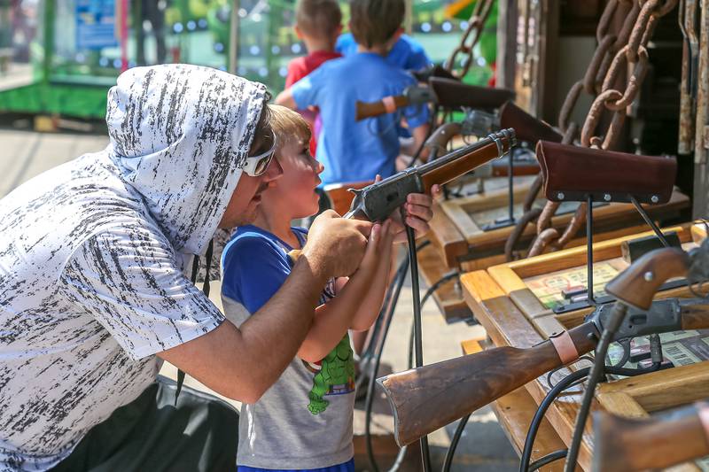 Michael Richter helps his son Ryan play a shooting game at the Downers Grove Rotary GroveFest in downtown Downers Grove. June 24, 2023.