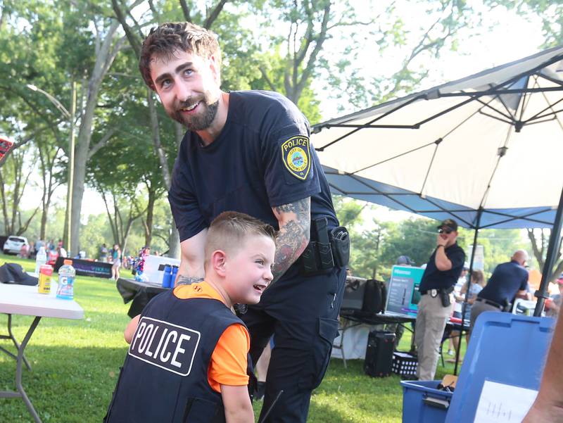 Spring Valley Police officer Mike Oslanzi places a police vest on Braxton Finley of Spring Valley, during the National Night Out event on Tuesday, Aug. 5, 2025 at Kirby Park in Spring Valley.  The event featured prizes, dodge ball tournamen, bounce house, face painting and more. National Night Out is an annual community policing campaign held on the first Tuesday of August to create police-community partnerships and build safer neighborhoods.