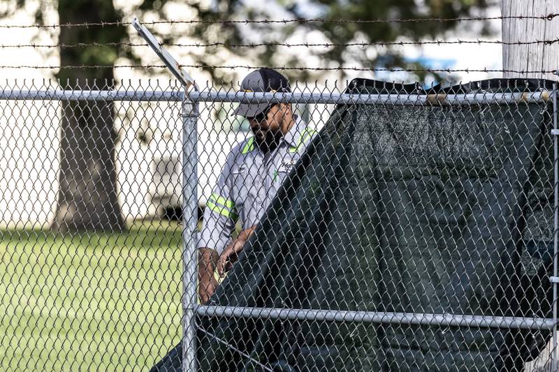 A contractor places black fabric along the fencing around the perimeter of the grounds of the Joliet Local Training Area site for the Illinois National Guard at 20612 Arsenal Road in Elwood on Wednesday, October. 8, 2025.