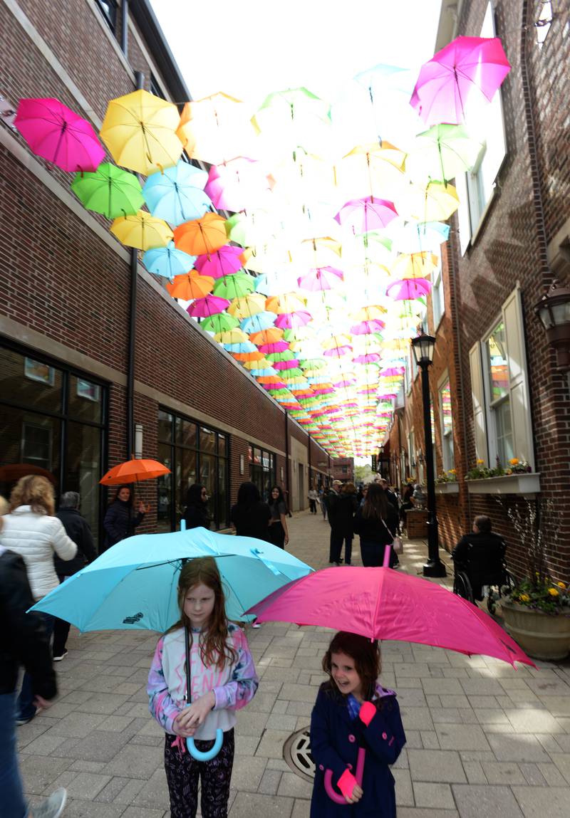 Children including (left) Anna (left) and Lily Horst of Naperville pose for photos while holding umbrellas during the Public Art Commission's Umbrella Sky Project Opening Day Party held Saturday April 29, 2023.