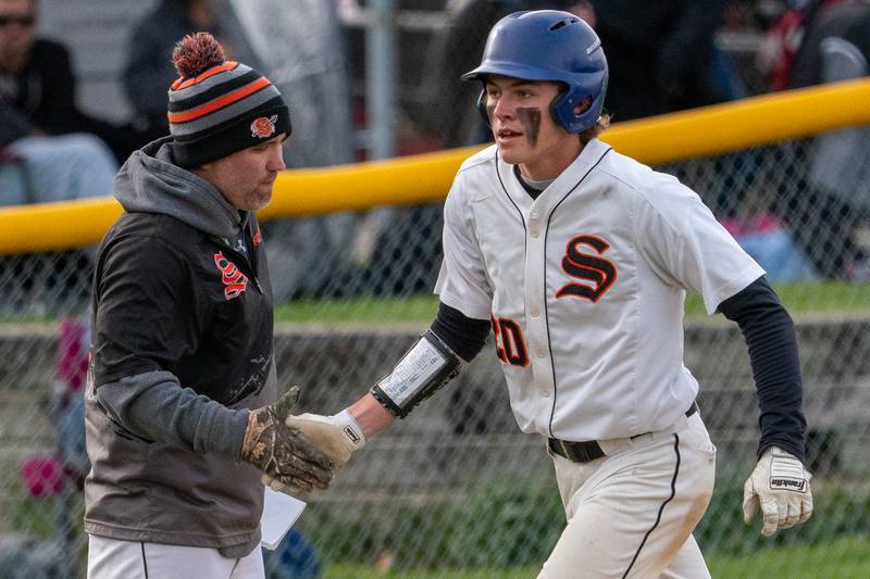 Sandwich’s Austin Marks (20) is greeted by Sandwich’s head coach Jason VanPelt after rounding third on a homer against Plano a baseball game at Sandwich High School on Monday, May 1, 2023.