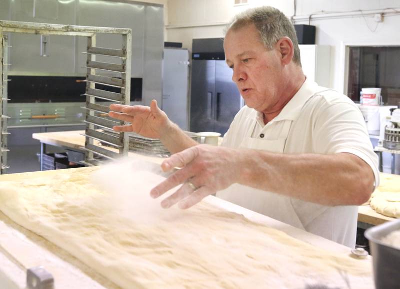 Ken Elleson, owner of Elleson's Bakery, applies flower to the dough before it is sliced up for paczkis Monday, Feb. 28, 2022, in the kitchen of the bakery in Sycamore. Elleson and members of his family will be working all night making the paczkis from scratch to be ready at 5 a.m. tomorrow for Fat Tuesday.