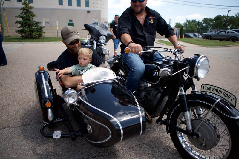 Sycamore boy Oilver Olinger, 2, and Dad Nathan Olinger, check out a sidecar with Andy Koczwara outside Sycamore Public Library Sunday, June 22, 2025. More than 100 bikers plus law enforcement escorted Olinger to the St. Charles Motorcycle Museum to celebrate the boy's cancer remission.