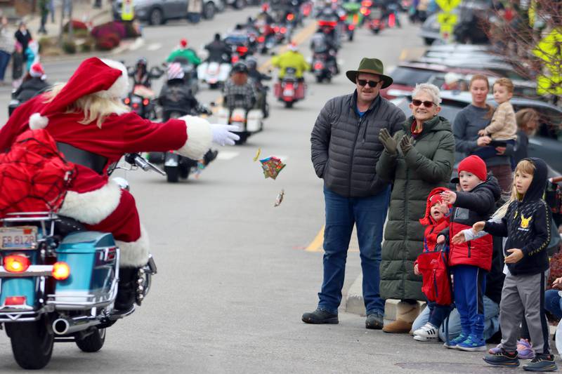 A motorcyclist tosses candy to children during the Toys for Tots Parade on Sunday, Nov. 24, 2024, in downtown McHenry.