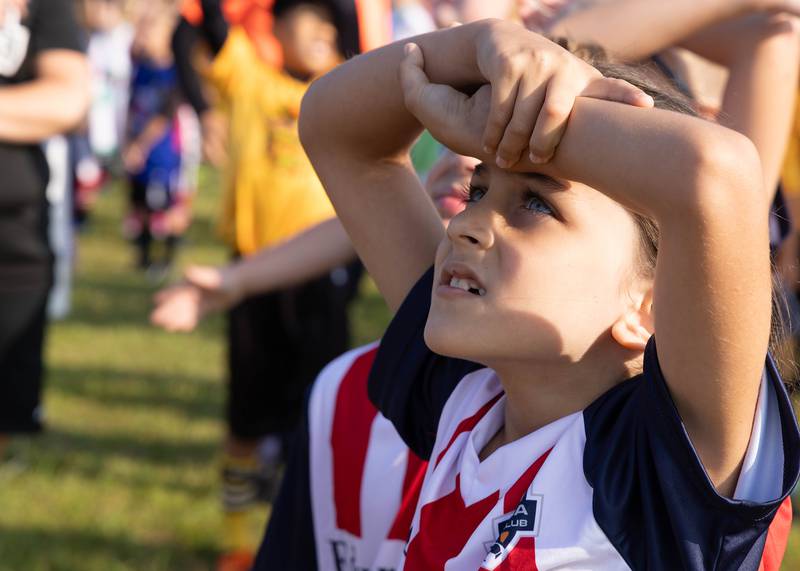 Players look to the sky Saturday, Aug. 19, 2023, as skydivers land at the East McKinley field in Ottawa during the Ottawa Youth Soccer opening day celebration.