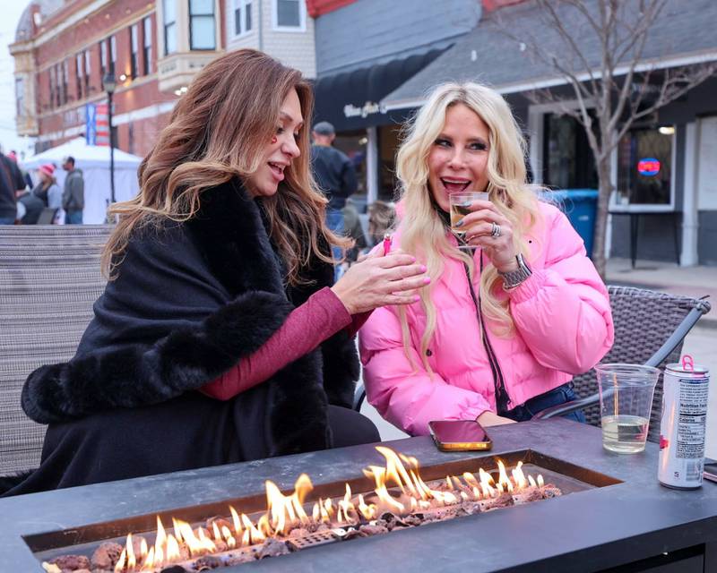 Rachael Glidic and Tera Sedivy enjoy wine by fire pit at the wine walk on Feb. 14, 2026 on Mill Street in Utica.
