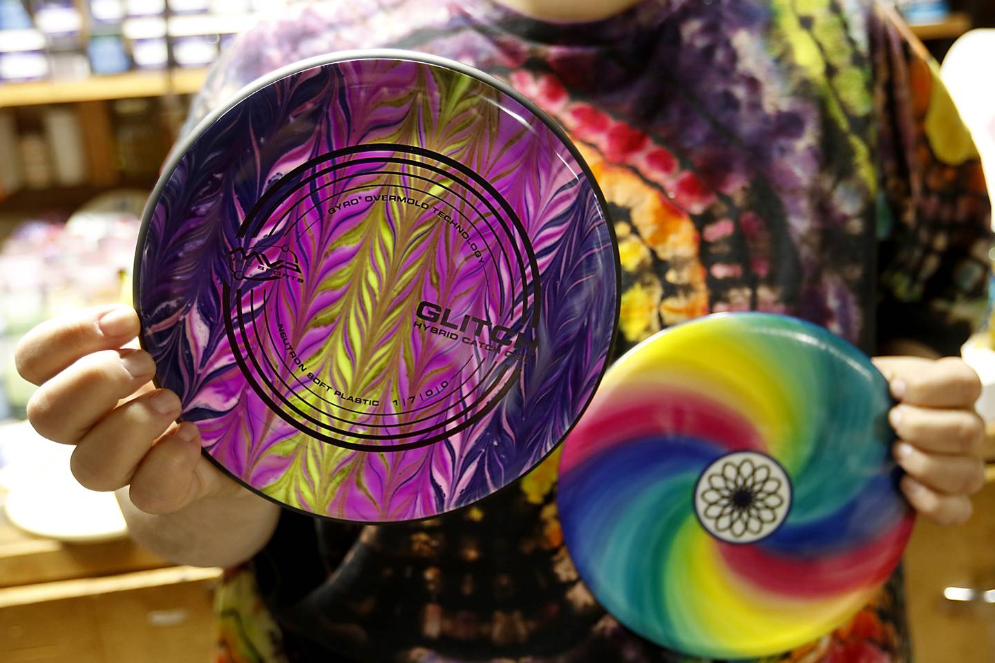 Mike Muggli holds two of his unique flying discs he creates on Wednesday, May 22, 2024, at his studios in his home in Crystal Lake.