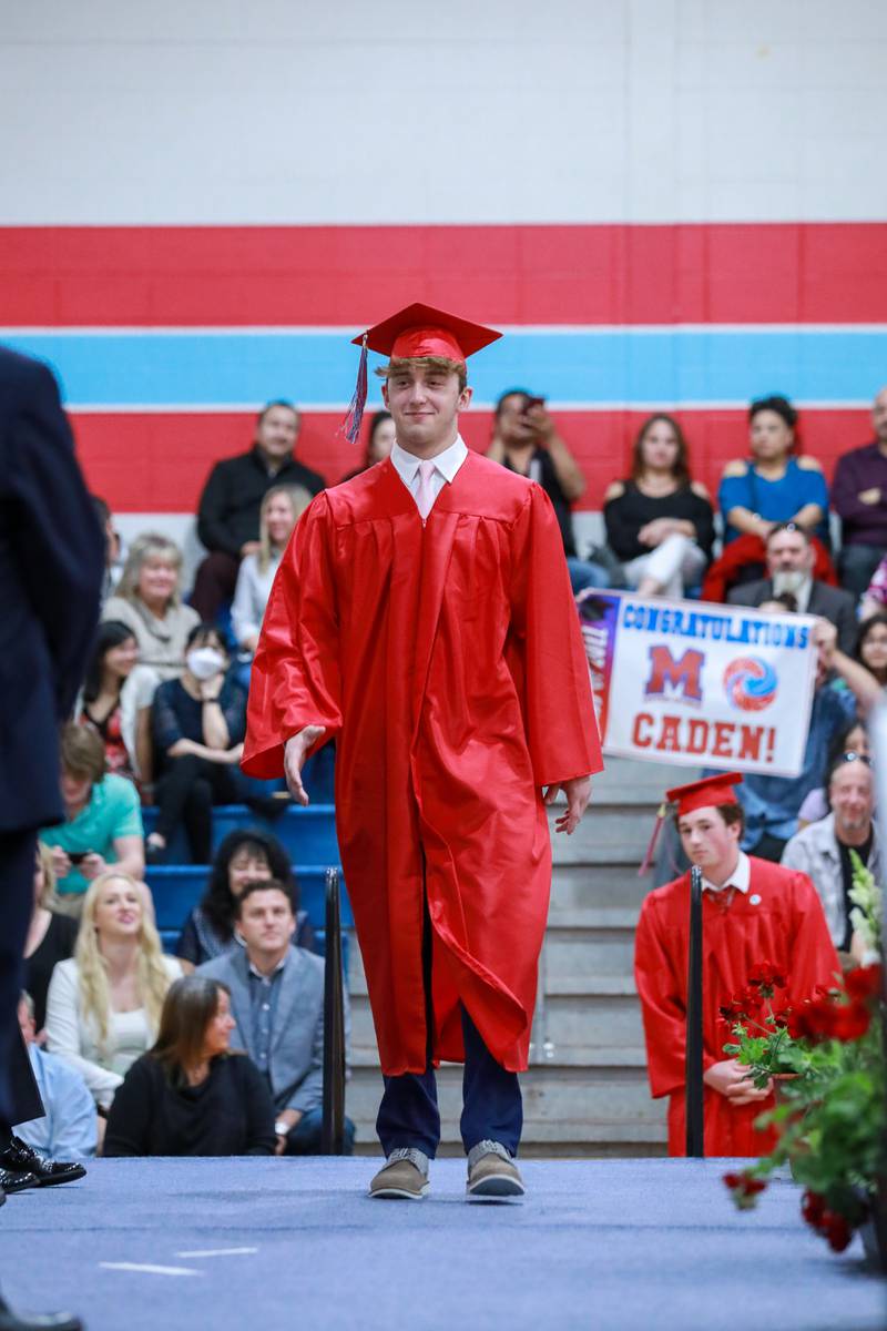 Caden Geils walks the stage to receive his diploma as family members wave a banner behind him Friday, May 27, 2022, during the Marian Central Catholic High School commencement ceremony.