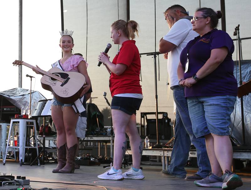 Bureau County Fair queen Kelsea Morgan holds an autographed guitar signed by Sara Evans and Josh Turner as Shaw Local Radio personalities Dani Holland and Caryn Brown announce on stage on Thursday, Aug. 24, 2023 at the Bureau County Fair in Princeton.