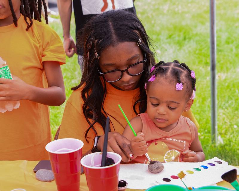 Imani, 14, helps her sister Emmarie Staine, of Cortland. paint a rock on Saturday, June 7, 2025, during the Ezra Hill Jr. Memorial Foundation’s 5th annual rock painting event held at Tyler Elementary School in DeKalb. The foundation was created to memorialize the late DeKalb boy, shot and killed in 2019.