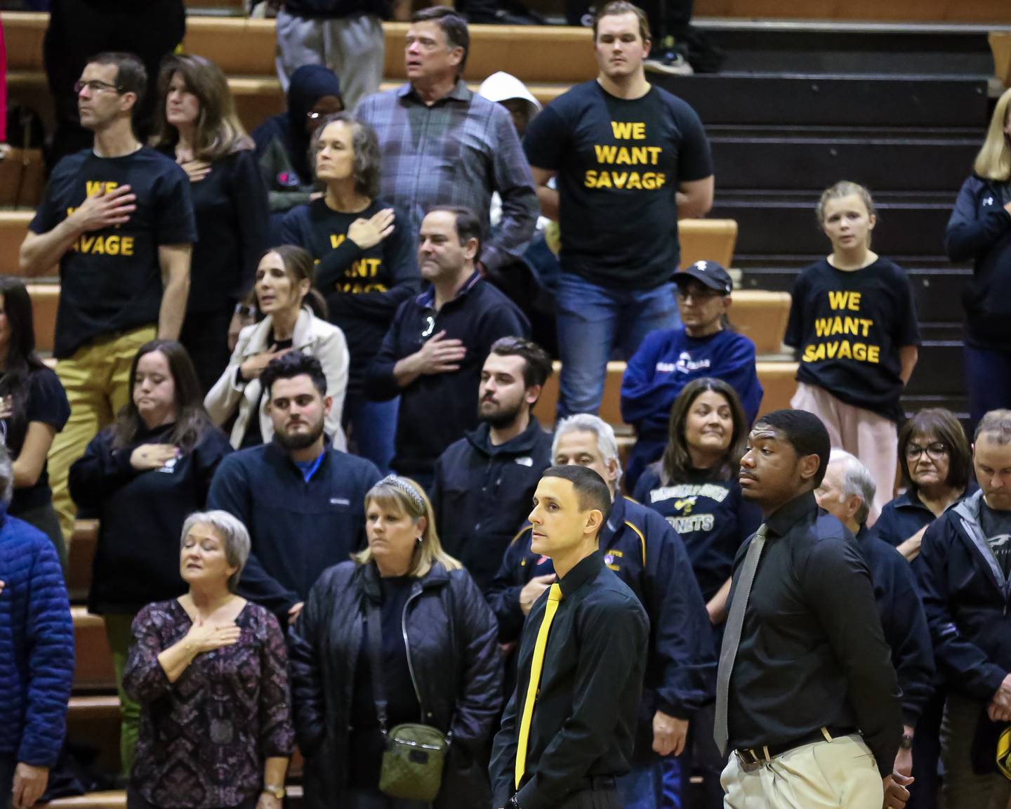 Hinsdale South's head coach Mike Belcaster stands for the playing of the national anthem with supporters of Hinsdale South's Brendan Savage in the background before basketball game between Hinsdale South at Downers Grove South. Dec 1, 2023.