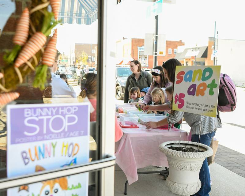 Community members make Sand Art outside of one of the Bunny Hop stop shops on Saturday April 12, 2025, during the annual bunny hop event in downtown Oswego.