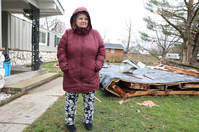 Connie Orozco stands near a portion of her roof in her front yard along South East Marquette Lane in Aroma Park on March 11, 2026 following a March 10 tornado that passed through Kankakee County.