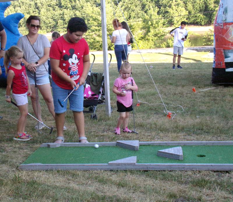 Analia Macias, of Spring Valley, watches a golf ball after striking it at the miniature golf course set up in the kids zone during the Rock the River celebration Sunday, July 3, 2022, along Water Street in Peru.