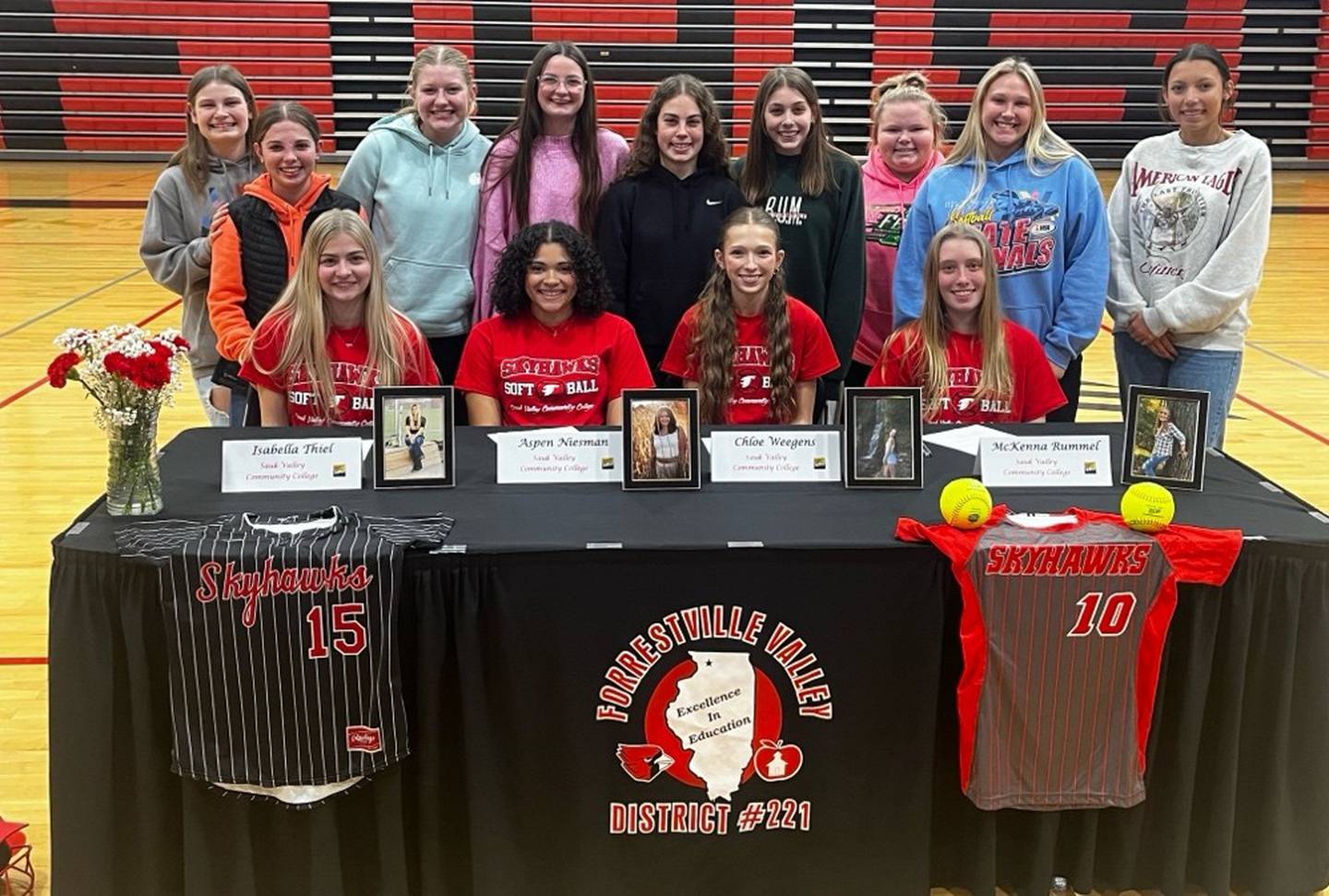 Isabella Thiel, Aspen Niesman, Chloe Weegen, and McKenna Rummel (seated, left to right) pose with members of the Cardinals softball team after announcing their intent to play for Sauk Valley College next school year.