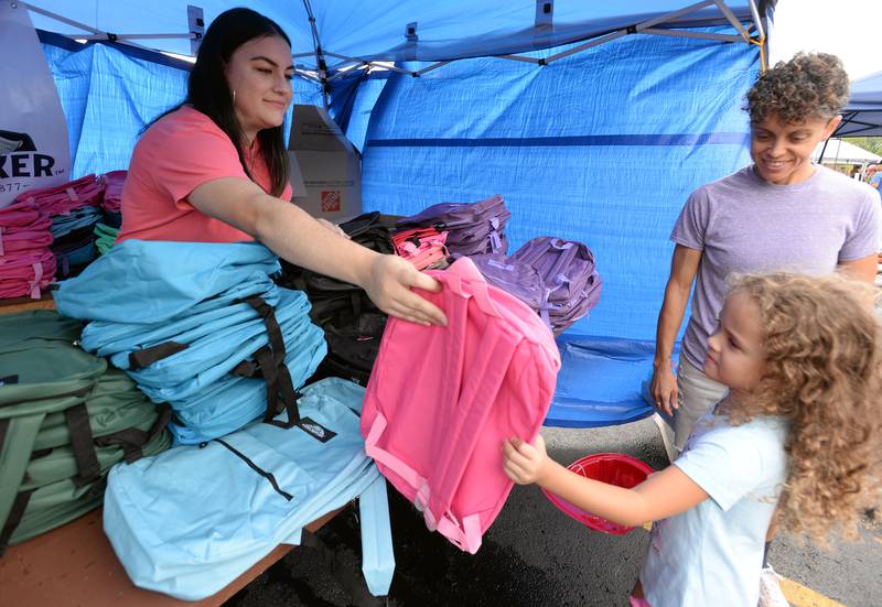La Grange city clerk Liz Saucedo hands out backpacks to children including Ruby Aguinaga of Countryside (beside Jenny Aguinaga) provided by Quaker Oats-PepsiCo during the District 105 Back to School/Neighborhood Fest held at Ideal Park Saturday Aug 20, 2022.