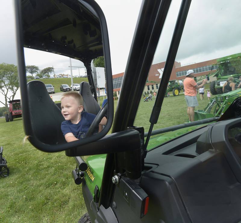 A happy Milo Norton is mirror reflected as he looks over the grounds of the Touch A Truck event Sunday, July 28, 2024, while pretending to drive a John Deere ATV in Ottawa.