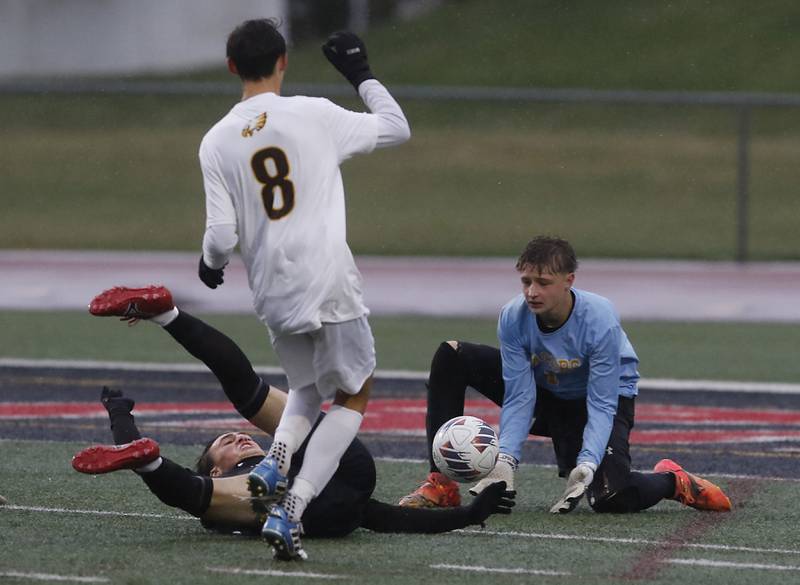Jacobs' Oskar Nowikowski fields the ball as Huntley's Max Connell crashes to the ground after being fouled by Jacobs' Anthony Rodriguez during an IHSA Class 3A Huntley Regional boys soccer semifinal match on Tuesday, Oct. 21, 2025, at Huntley High School.