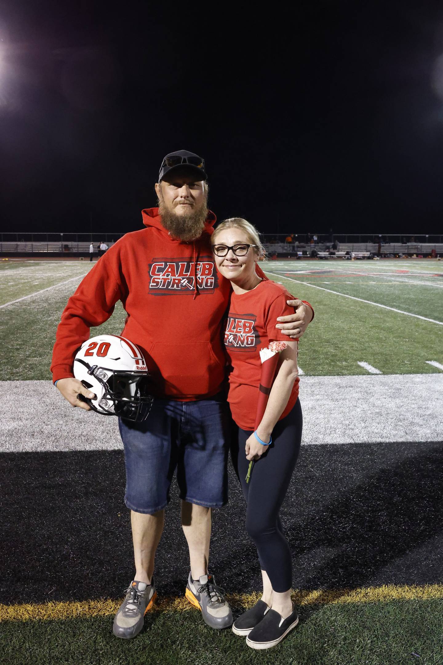Nick and Jennifer Outerbridge pose for a photo with their son Caleb's helmet as they attended the Bradley-Bourbonnais Community High School football team's senior night celebration in October 2025.