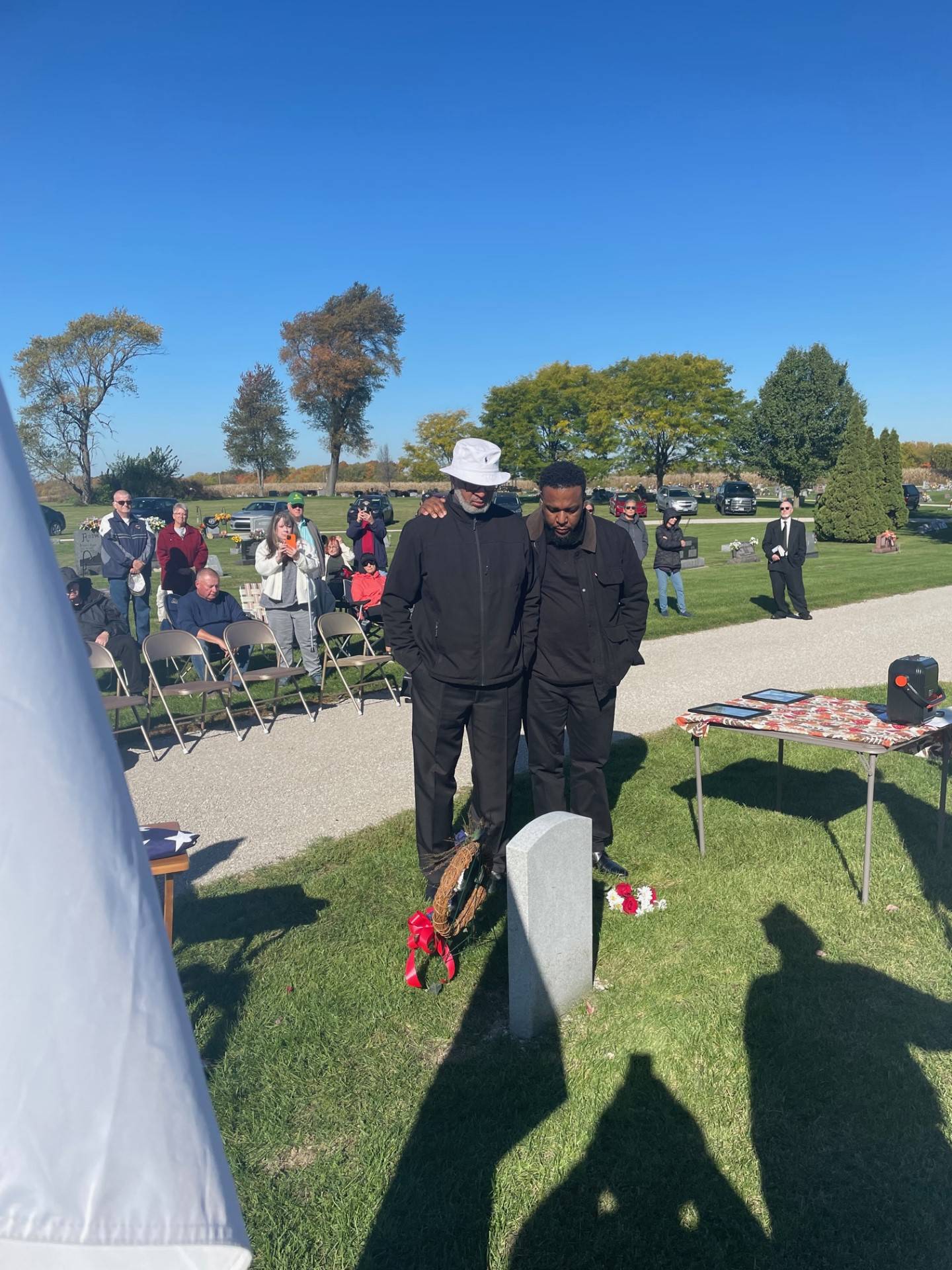 Toby Reddick Sr. (wearing a white hat) and son Toby Reddick Jr. share a solemn moment Saturday, Oct. 21, 2023, at Granville Cemetery, over the grave of America Reddick is laid to rest. America Reddick, Toby Sr.'s great-grandfather, was a former slave and Civil War soldier whose grave now is graced with a military marker.