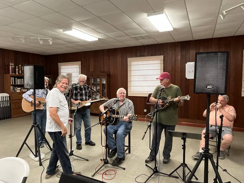Mike Bratt is First Fridays’ sound man as well as a performer. He’s seen here in the white t-shirt, setting up for, from left to right, Larry Wallace on dobro, Jerry Tice on guitar, Tracy Fleck on mandolin, and Randy Holland on harmonica. Lowell Harp, on guitar, is in the background.