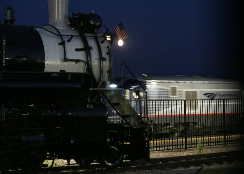 A nearly full supermoon appears above the 2-8-2 Mikado class engine as an Amtrak train passes behind on Tuesday, Aug. 29, 2023 at the Union Depot Railroad Museum in Mendota. The first full Moon came on August 2 and the second one on August 30.