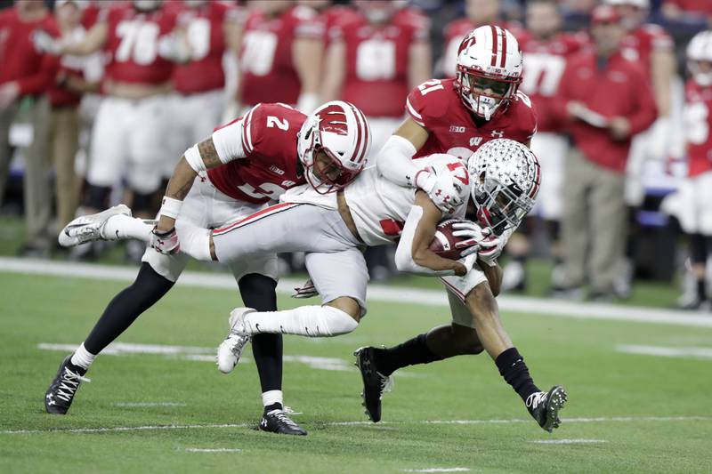 FILE - Ohio State wide receiver Chris Olave (17) is tackled by Wisconsin safety Reggie Pearson (2) and cornerback Caesar Williams (21) during the second half of the Big Ten championship NCAA college football game Saturday, Dec. 7, 2019, in Indianapolis.  Ohio State annually boasts one of the nation’s highest-scoring offenses. Wisconsin traditionally has one of the stingiest defenses in the land. Yet the two Big Ten programs don’t get a chance to face each other every year because they’re in separate divisions. These two strong units look forward to facing off Saturday, Sept. 24, 2022, when the Badgers visit the third-ranked Buckeyes. (AP Photo/Michael Conroy, File)