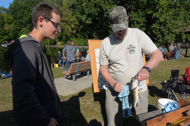 Christopher Holcomb, 13, of Sterling turn the bass he caught to David Schipper, retired Whiteside County Sheriff employee, during the sheriff department's annual fishing derby at Morrison-Rockwood State Park in Morrison on Saturday, Sept. 9, 2023.