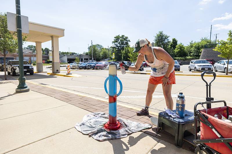 Nora Reuter puts a base coat on Superman Monday, June 24, 2024 in Dixon. Reuter has been painting bike posts in the downtown, unveiling their super identities.