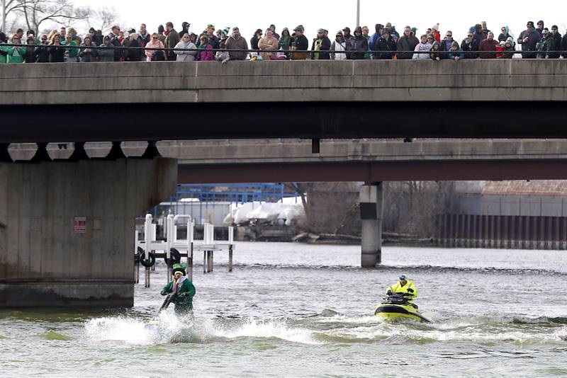 People watch from a bridge as a jet skier, dressed as a leprechaun stirs dye into the Fox River, as the river is dyed green during the ShamROCKS the Fox Festival in McHenry on Saturday, March 16, 2024.