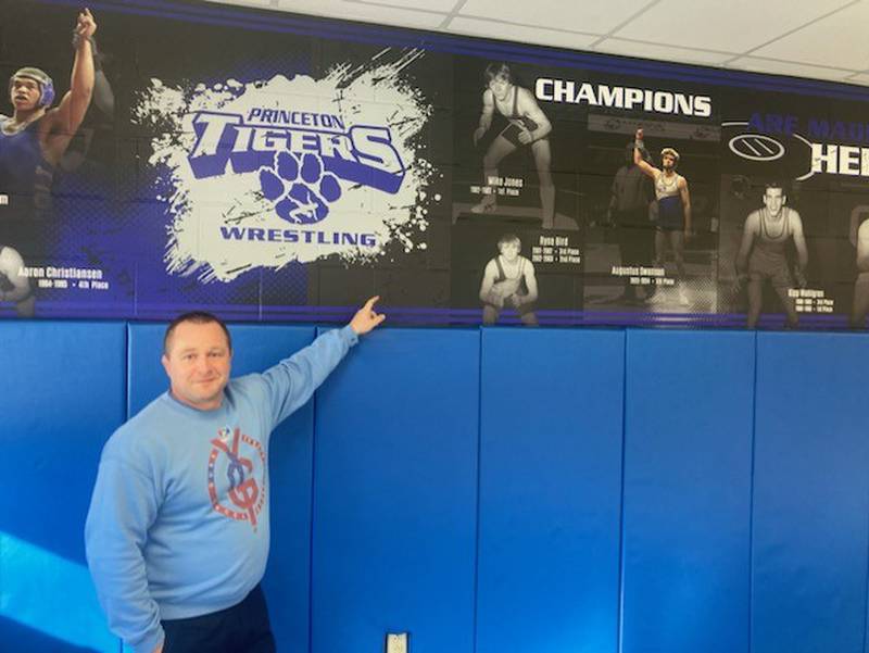Princeton Tiger wrestling coach shows the new murals of Tiger state medalist painted on the wall of the PHS wrestling room.