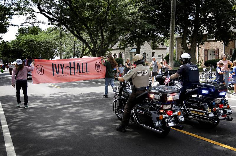 Law enforcement offices on motorcycles fallow the Ivy-Hall dispensary banner on Sunday, July 6, 2024, during Crystal Lake’s annual Independence Day Parade on Dole Avenue in Crystal Lake.