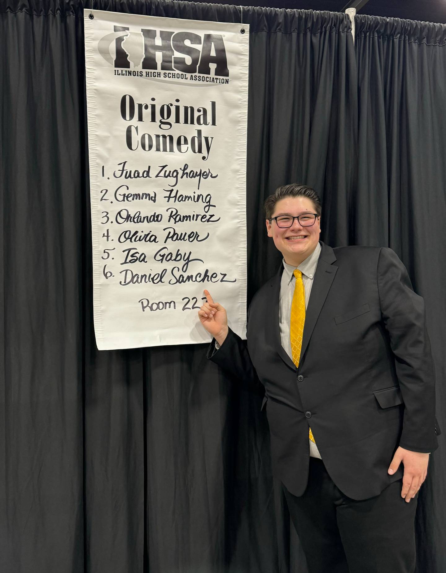 Joliet West Senior Daniel Sanchez stands with the poster announcing the six finalists in Original Comedy at the IHSA State Speech tournament.
