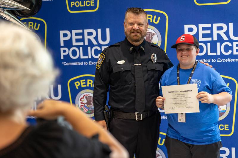 (left to right) Jen Heredia takes photo of Officer Brian Zebron and Junior Police Cadet Levi Petersen at the first annual Juvenile Police Academy graduation ceremony on Friday, July 25, 2025 at the Peru Police Department in Peru.