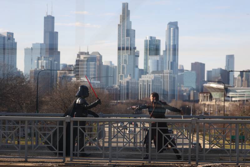 Two Star Wars cosplayers have a lightsaber fight along a Chicago skyline backdrop walkway at C2E2 Chicago Comic & Entertainment Expo on Sunday, April 2, 2023 at McCormick Place in Chicago.