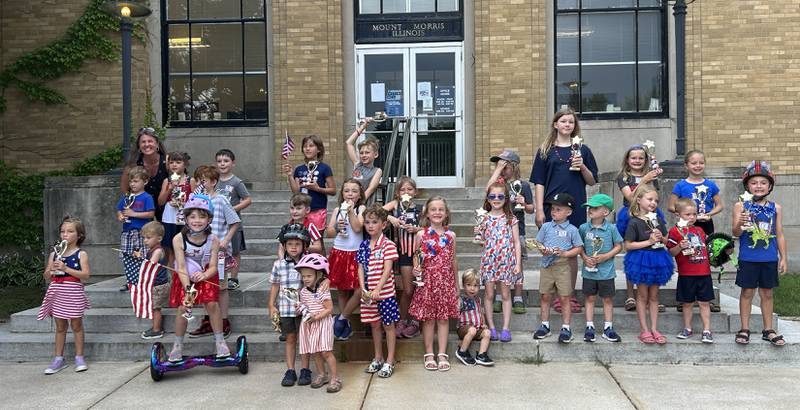 Kids who took part in the the Let Freedom Ring Kiddie Parade on Saturday, July 5, 2025 stand on the steps of the Mt. Morris Post Office with Rockford meteorologist Candice King.