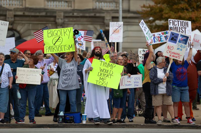 Elijah Brill, center, of Manteno, dresses as Jesus holding a sign commenting on immigration during the No Kings Rally at the Kankakee County Courthouse on Saturday, Oct. 18, 2025.