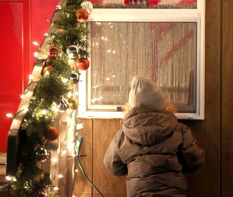 A child peeks in the window of the Santa house near the Egyptian Theatre Thursday, Dec. 1, 2022, during the DeKalb Chamber of Commerce Lights on Lincoln and Santa Comes to Town.
