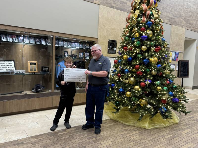 Kash P. from Morris Elementary School hands Jeff Poundstone from Disabled American Veterans a check for $500.