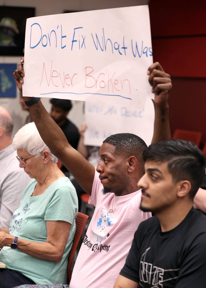 Audience members hold signs Monday, June 23, 2025, opposed to amending the city code to prohibit the sale of illicit THC products and kratom within DeKalb during the city council meeting at the DeKalb Public Library.