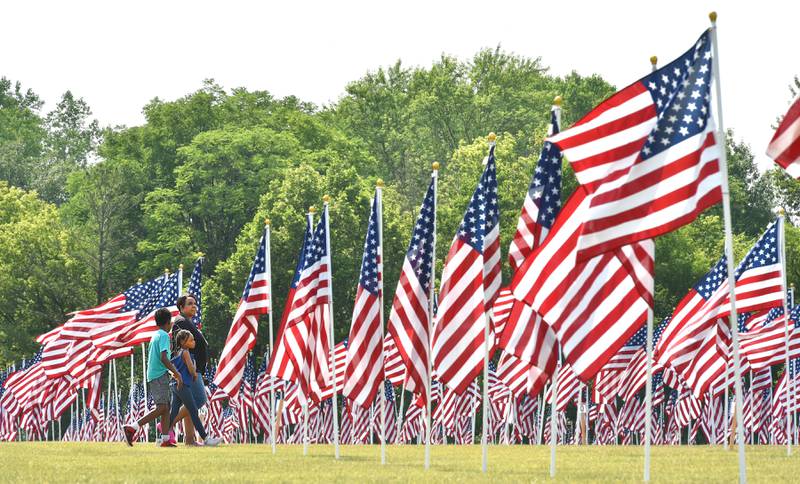 Ezekiel Spencer, 11, his sister Liberty, 8 and their mother Tonya Spencer of Naperville, walks through The Field of Honor on display at Seven Gables Park in Wheaton Monday, July 3, 2023. Each of the 2,000 American Flags may be sponsored by individuals or groups who can tie a note to the pole to honor individuals or groups.