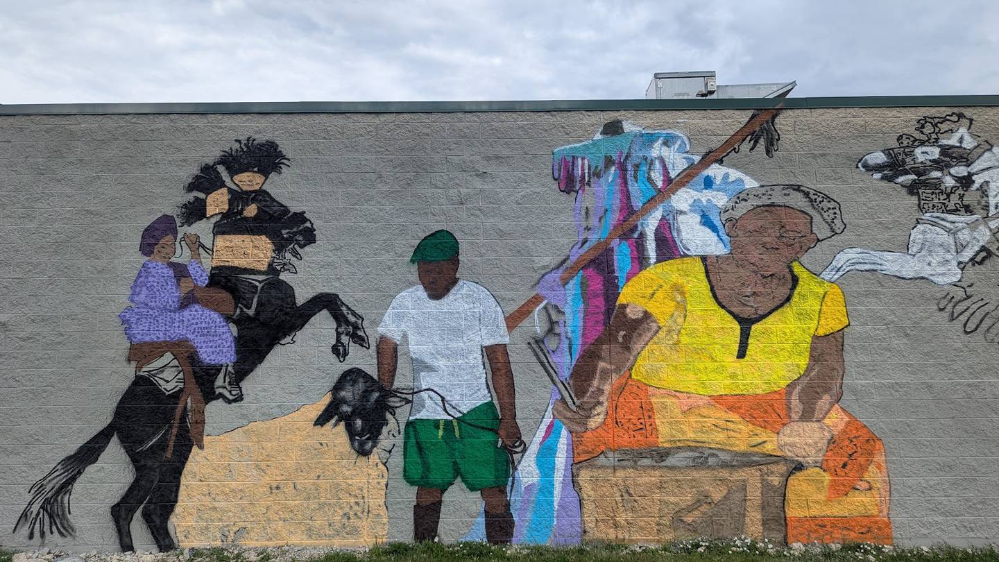 A mural-in-progress on the side of the future O’Larry Asun Spot, a restaurant that will feature West African dishes, is seen on Friday, June 20, 2025, at 3109 Theodore St. in Joliet. Jelili “Larry” Olaniyan, the restaurant’s owner, hired The artist is Uprizn Ikpemi, 40, of South Holland, a Nigerian-born American visual artist, muralist and art teacher, to paint the mural. This section features a woman cooking a traditional West African dish and Olaniyan holding a goat, which symbolizes the traditional cuisine the restaurant will serve.